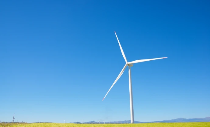 Large wind turbine against a blue sky in a light green field of wheat.